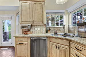 Kitchen with a wealth of natural light, decorative backsplash, stainless steel dishwasher, and light brown cabinets