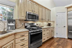 Kitchen featuring dark wood-type flooring, light stone countertops, tasteful backsplash, light brown cabinets, and stainless steel appliances