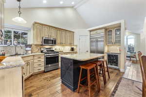 Kitchen with decorative backsplash, appliances with stainless steel finishes, wine cooler, and a kitchen island