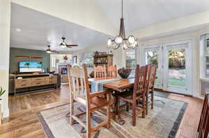 Dining area with ceiling fan with notable chandelier, lofted ceiling, and wood-type flooring