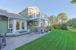 Rear view of house with a lawn, a balcony, and a patio