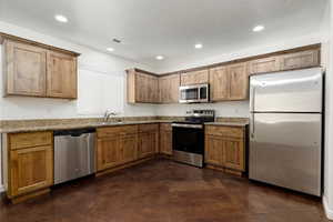 Kitchen featuring sink, stainless steel appliances, dark tile patterned floors, stamped dark brown concrete floor, white painted walls, and light granite countertops