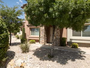 Front entrance of home with stucco, stone, sidewalk, rocks and trees