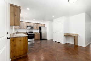 Kitchen featuring sink, stainless steel appliances, stamped, dark brown concrete flooring, white painted walls, and light stone countertops