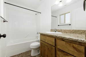 Primary full bathroom featuring white painted walls, vinyl, tile looking, patterned flooring, toilet, vanity, and bathtub / shower combination