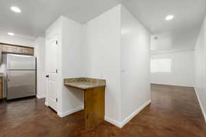 Hallway between kitchen with desk and living room and stamped, dark brown concrete flooring