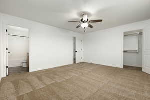 Unfurnished primary bedroom with white painted walls, carpet flooring, ceiling fan, a closet, and ensuite bathroom