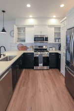 Kitchen with sink, light wood-type flooring, appliances with stainless steel finishes, tasteful backsplash, and white cabinetry