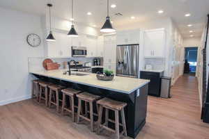 Kitchen with decorative backsplash, pendant lighting, white cabinetry, light hardwood / wood-style floors, and stainless steel appliances