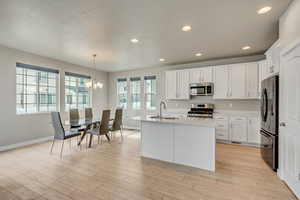 Kitchen with light wood-type flooring, a kitchen island with sink, white cabinets, appliances with stainless steel finishes, and sink