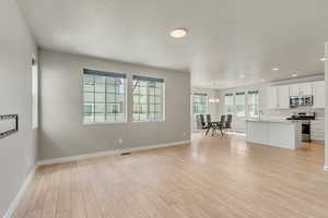 Unfurnished living room with sink, a notable chandelier, light hardwood / wood-style flooring, and a textured ceiling