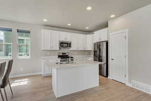 Kitchen with white cabinets, light hardwood / wood-style flooring, appliances with stainless steel finishes, and an island with sink