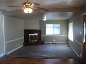 Unfurnished living room with ceiling fan, wood-type flooring, and a brick fireplace