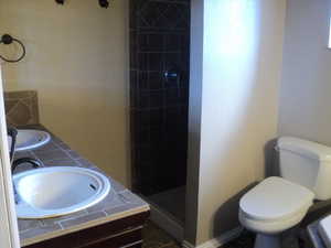 Bathroom featuring toilet, a tile shower, and vanity