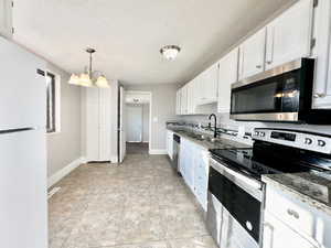 Kitchen with chandelier.  Stainless steel appliances.  Granite countertops.  White cabinets.  White refrigerator.  Light tile patterned floors.