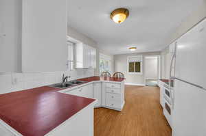 Kitchen with light hardwood / wood-style floors, tasteful backsplash, sink, white cabinets, and white appliances