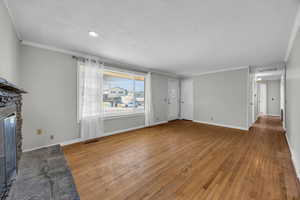 Unfurnished living room featuring a fireplace, a textured ceiling, light hardwood / wood-style floors, and ornamental molding