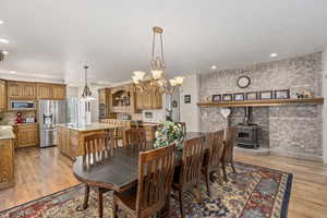 Dining room with an inviting chandelier, light hardwood / wood-style floors, brick wall, and a wood stove