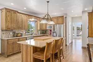 Kitchen with backsplash, hanging light fixtures, light hardwood / wood-style flooring, a kitchen island, and stainless steel appliances