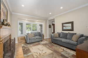 Living room featuring light wood-type flooring, crown molding, and a high end fireplace