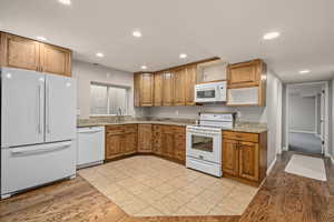 Kitchen with sink, light hardwood / wood-style flooring, light stone counters, and white appliances