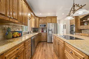 Kitchen with backsplash, stainless steel appliances, light hardwood / wood-style floors, sink, and light stone countertops