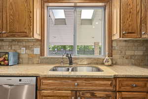 Kitchen with backsplash, dishwasher, a skylight, sink, and light stone countertops