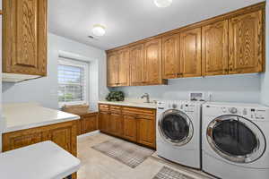 Laundry room featuring light tile patterned floors, sink, washing machine and clothes dryer, and cabinets