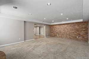 Carpeted spare room with a textured ceiling and brick wall