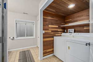 Washroom with wood walls, wooden ceiling, light tile patterned floors, and washer and dryer