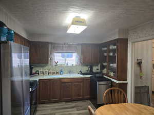 Kitchen featuring dark brown cabinets, light hardwood / wood-style floors, stainless steel refrigerator, tasteful backsplash, and black electric range oven