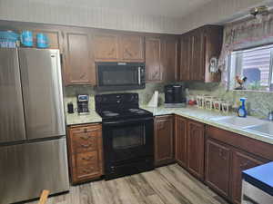 Kitchen featuring dark brown cabinets, sink, tasteful backsplash, black appliances, and light wood-type flooring