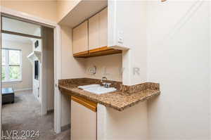 Kitchen featuring light colored carpet, sink, and light stone counters