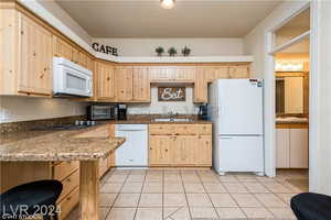 Kitchen with light brown cabinetry, white appliances, and light tile patterned floors