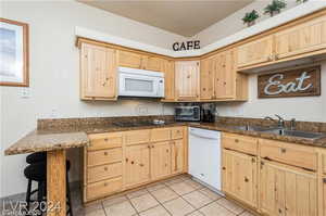 Kitchen featuring light tile patterned flooring, a kitchen bar, sink, white appliances, and light brown cabinetry