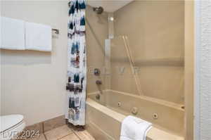 Bathroom with tile patterned floors, shower / bath combo with shower curtain, and toilet