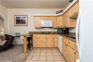 Kitchen with light tile patterned floors, a breakfast bar area, white appliances, and light brown cabinetry