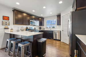 Kitchen with a kitchen breakfast bar, dark brown cabinetry, hardwood / wood-style flooring, kitchen peninsula, and stainless steel appliances