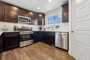 Kitchen with appliances with stainless steel finishes, dark wood-type flooring, sink, and dark brown cabinets