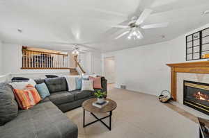 Living room featuring ceiling fan, a tiled fireplace, and light carpet