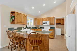 Kitchen featuring a kitchen breakfast bar, high vaulted ceiling, sink, kitchen peninsula, and white appliances