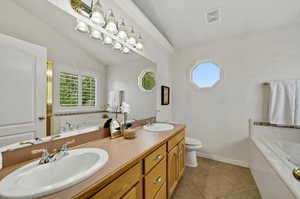 Bathroom featuring tiled tub, vaulted ceiling, vanity, and toilet