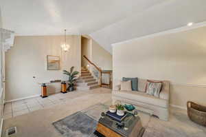 Carpeted living room featuring high vaulted ceiling, a notable chandelier, and ornamental molding