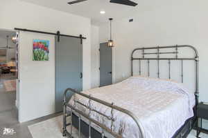 Bedroom with ceiling fan, a barn door, and concrete floors