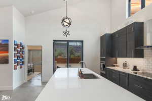 Kitchen featuring black electric stovetop, backsplash, high vaulted ceiling, hanging light fixtures, and sink