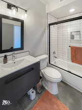 Full bathroom featuring concrete flooring, combined bath / shower with glass door, toilet, and vanity