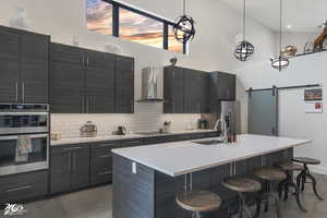 Kitchen featuring sink, wall chimney exhaust hood, a kitchen island with sink, tasteful backsplash, and stainless steel appliances