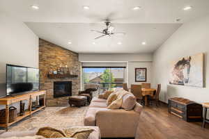 Living room with ceiling fan, vaulted ceiling, hardwood / wood-style floors, and a stone fireplace