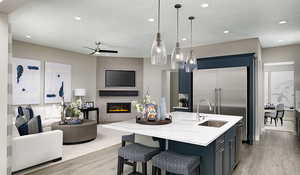 Kitchen with ceiling fan, light wood-type flooring, a large fireplace, sink, and a center island with sink