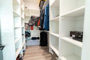 Walk in closet with light hardwood / wood-style floors